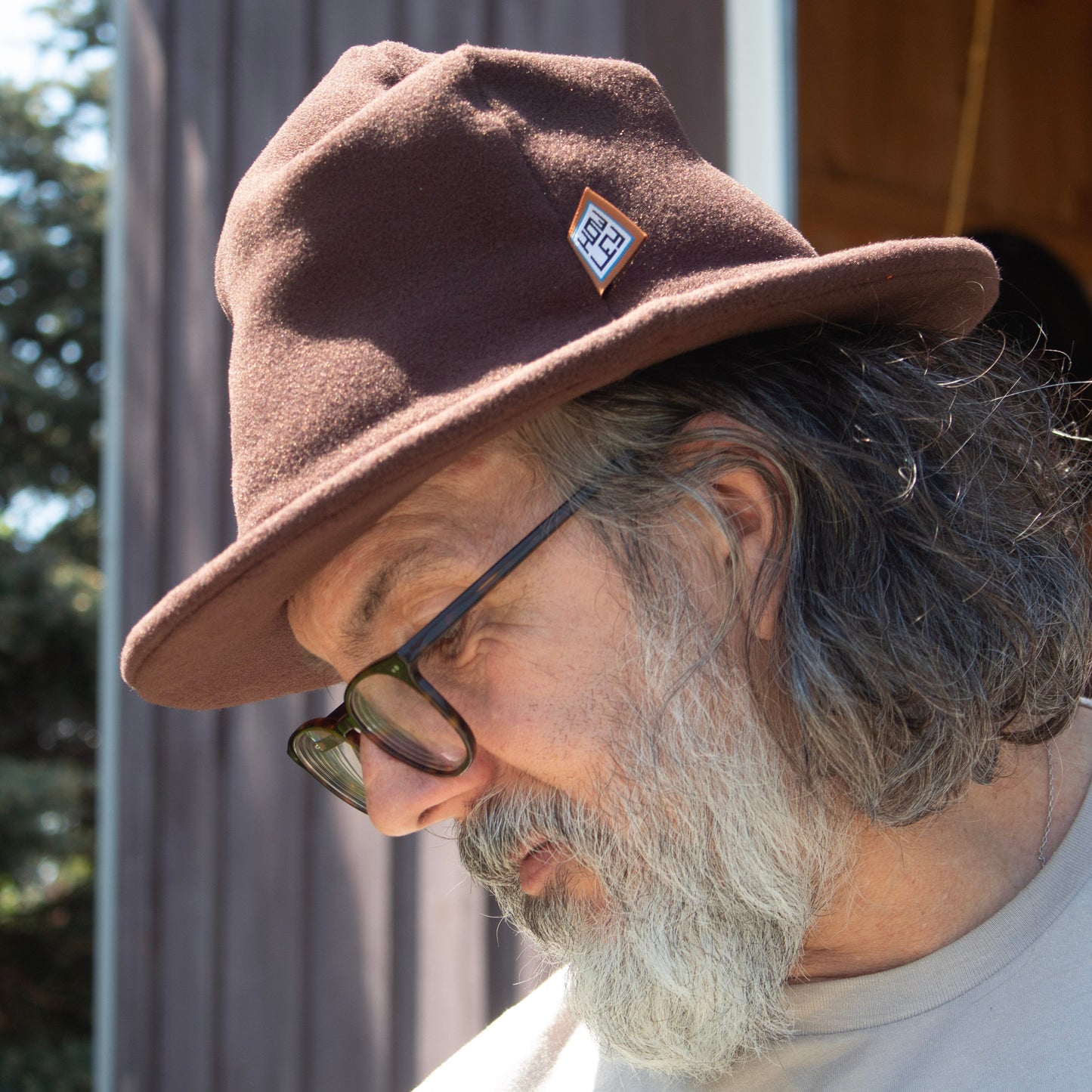 Man wearing a brown Howley hat with a logo, glasses, and a white shirt with blue text.
