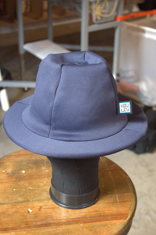 A blue Howley brimmed hat displayed on a black mannequin head stand on a wooden table.
