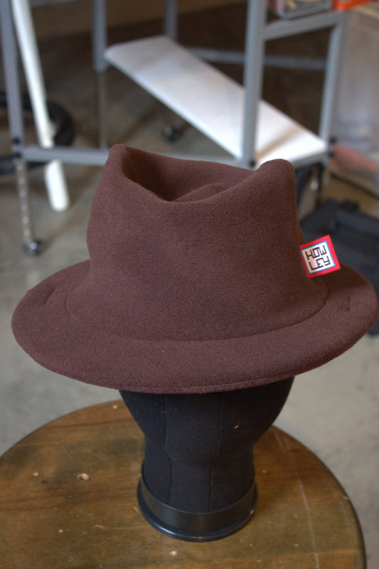 A Howley brimmed hat displayed on a black mannequin head, set on a wooden table with a blurred workshop background.