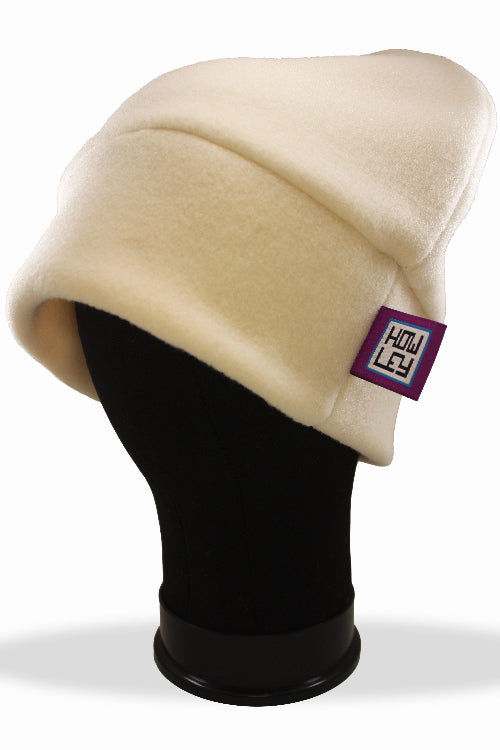 Beige beanie on a black mannequin head with a purple tag featuring a logo.