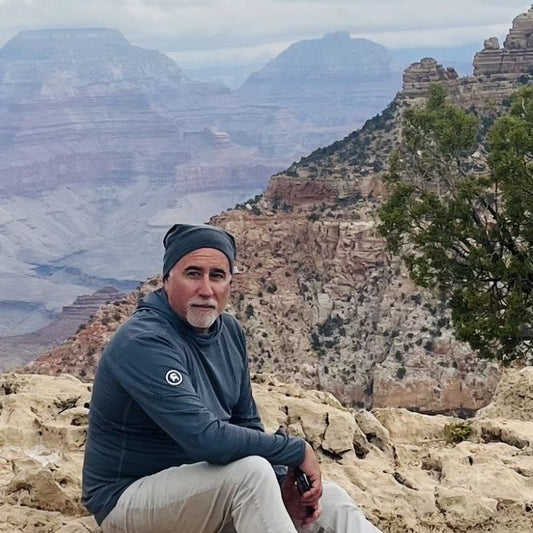 Man sitting on a rocky outcrop with a scenic view of the Grand Canyon.