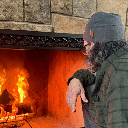 Person leaning against a stone fireplace with a warm fire inside