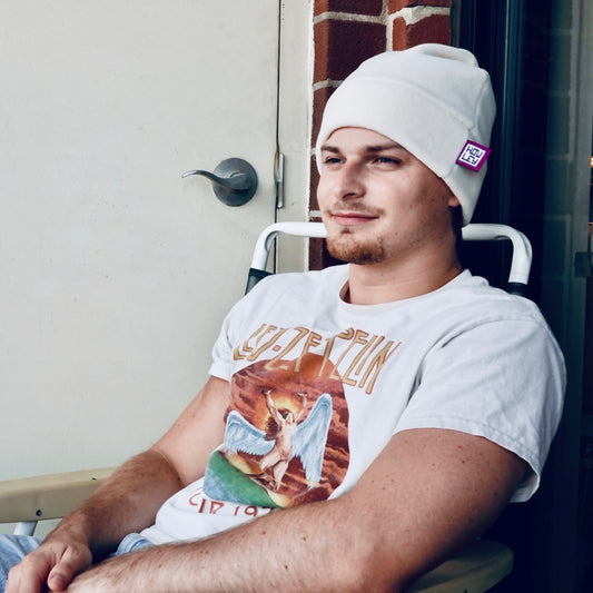Person wearing a white beanie and graphic t-shirt sitting on a chair.